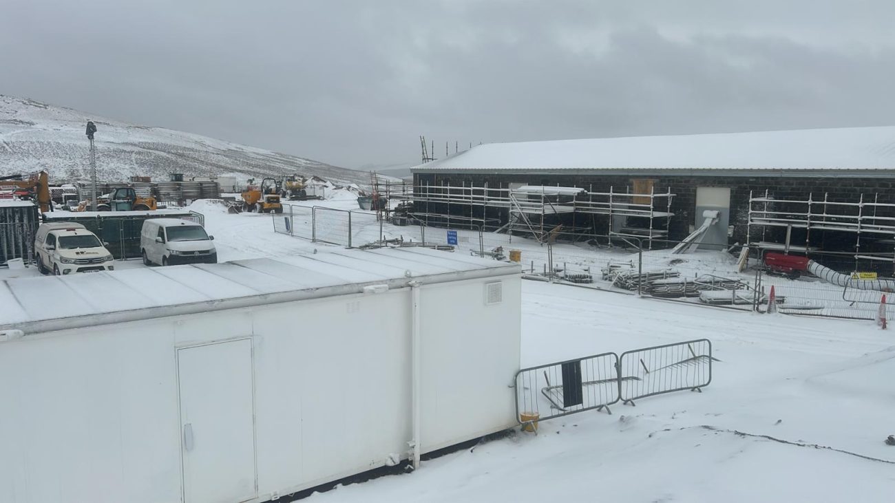 Construction continuing on the Hagshaw Hill Windfarm control building during severe winter conditions, with the site covered in snow across the surrounding hillside.